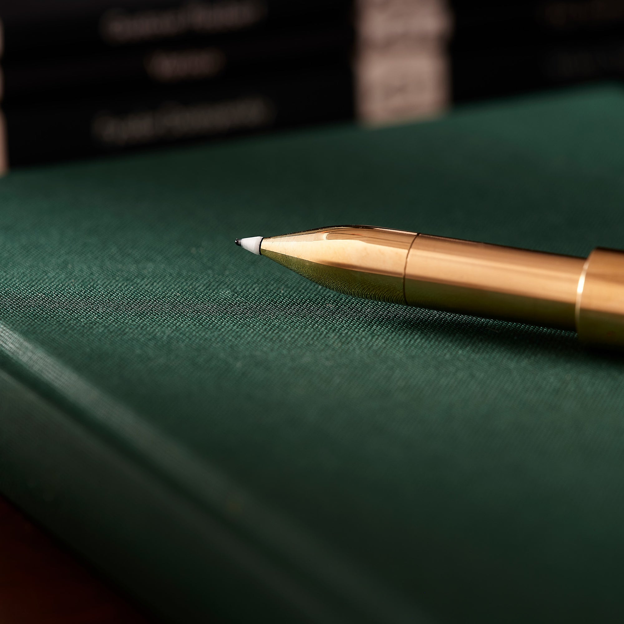 Close-up of the Brass Wren refillable writing pen’s tip, lying on a green notebook with book spines blurred in the background.