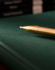 Close-up of the Brass Wren refillable writing pen’s tip, lying on a green notebook with book spines blurred in the background.