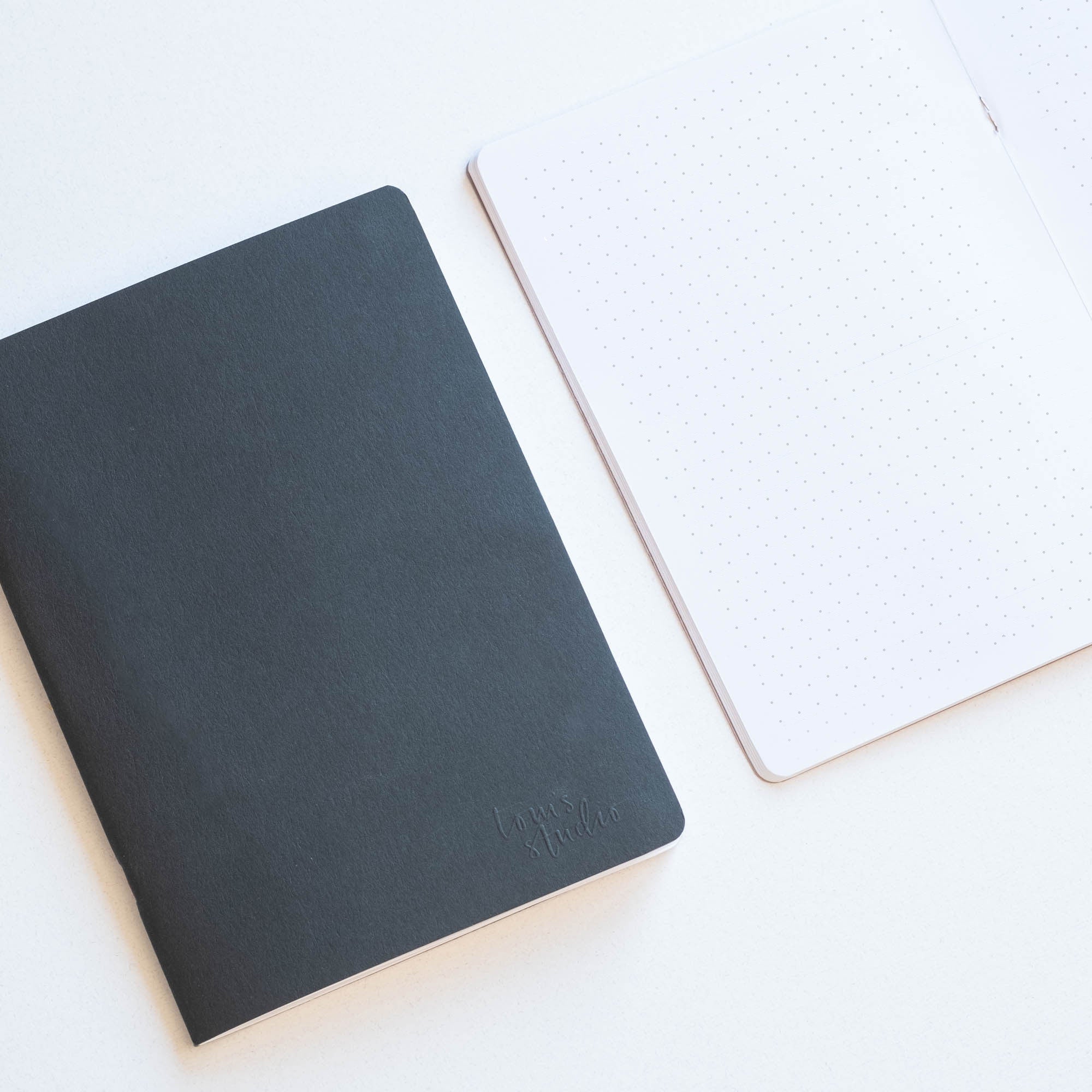 Two Tom's Studio A5 coffee cup notebooks sitting side by side on a table, a black covered notebook is shut and the other open.