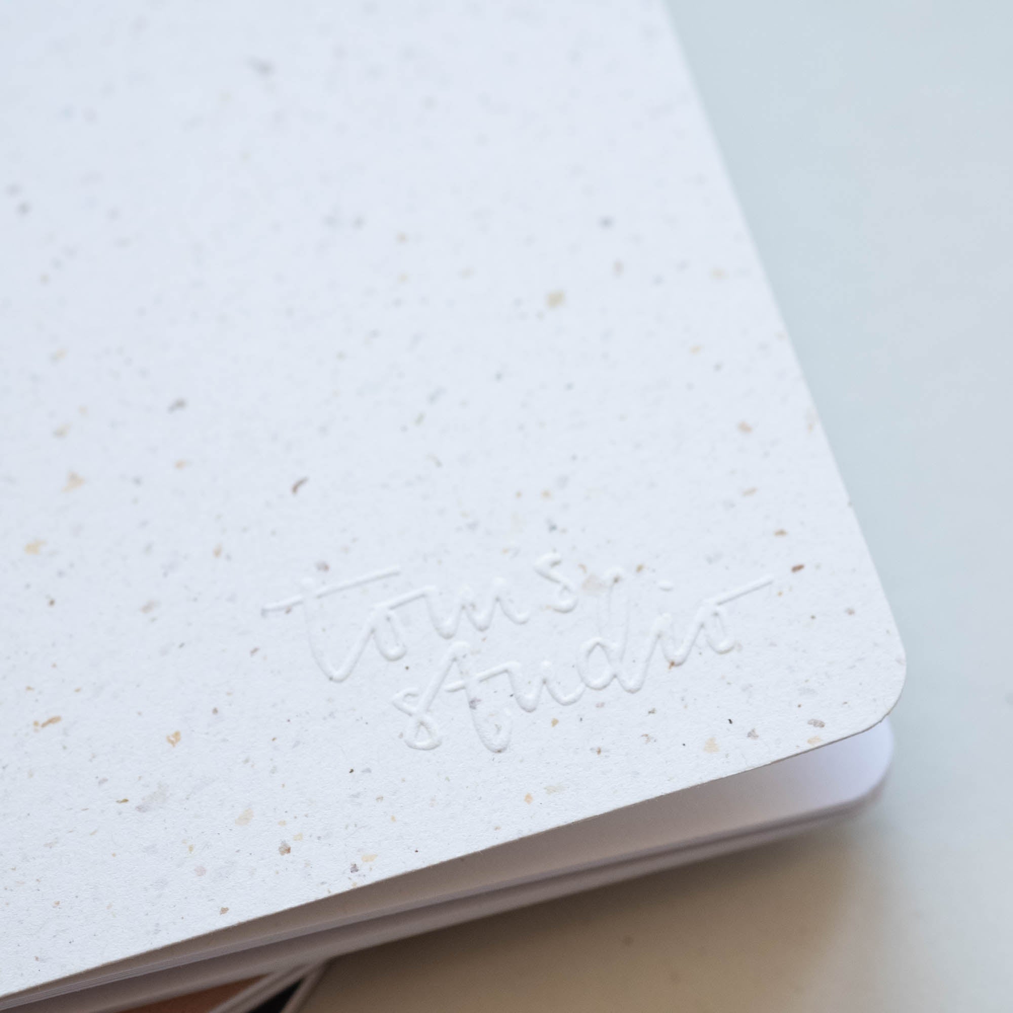 Detail of embossed logo on Tom's Studio x Coffeenotes A5 Notebook in 'Grounds' (white), made from recycled coffee cups and eco-friendly materials.