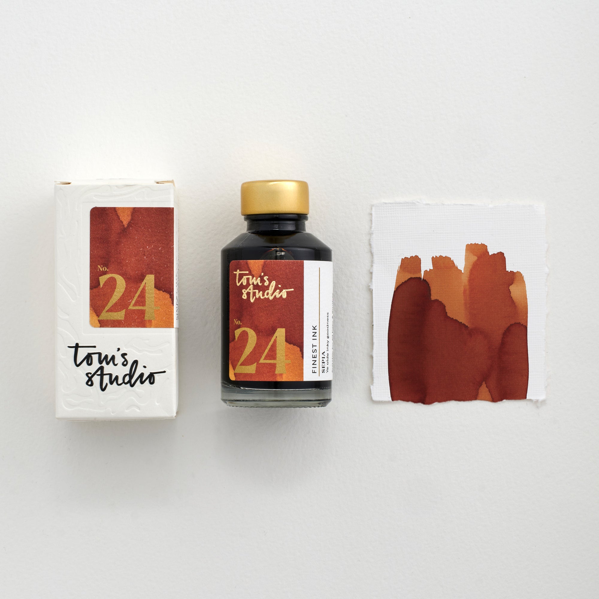 Tom's Studio Sepia Fountain Pen Ink – bottle with gold lid, boxed packaging featuring a brown and gold label marked '24', and a swatch of the brown ink on textured paper.