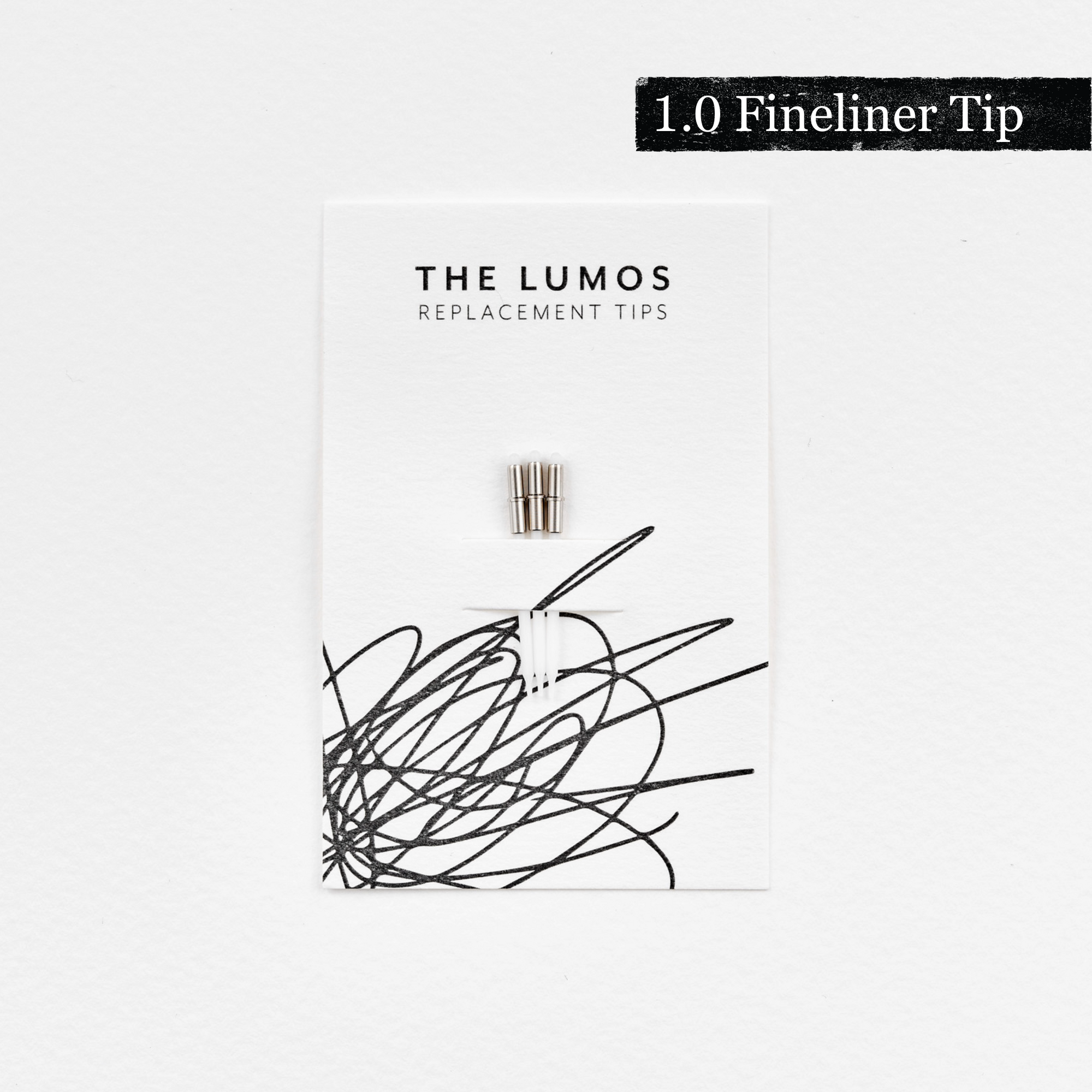 A pack of three Lumos 1.0mm fineliner replacement tips attached to a white backing card. The card features 'THE LUMOS REPLACEMENT TIPS' in uppercase black letters at the top, with an abstract black ink scribble design in the lower half. A black textured label in the upper right corner displays '1.0 Fineliner Tip' in white text. 