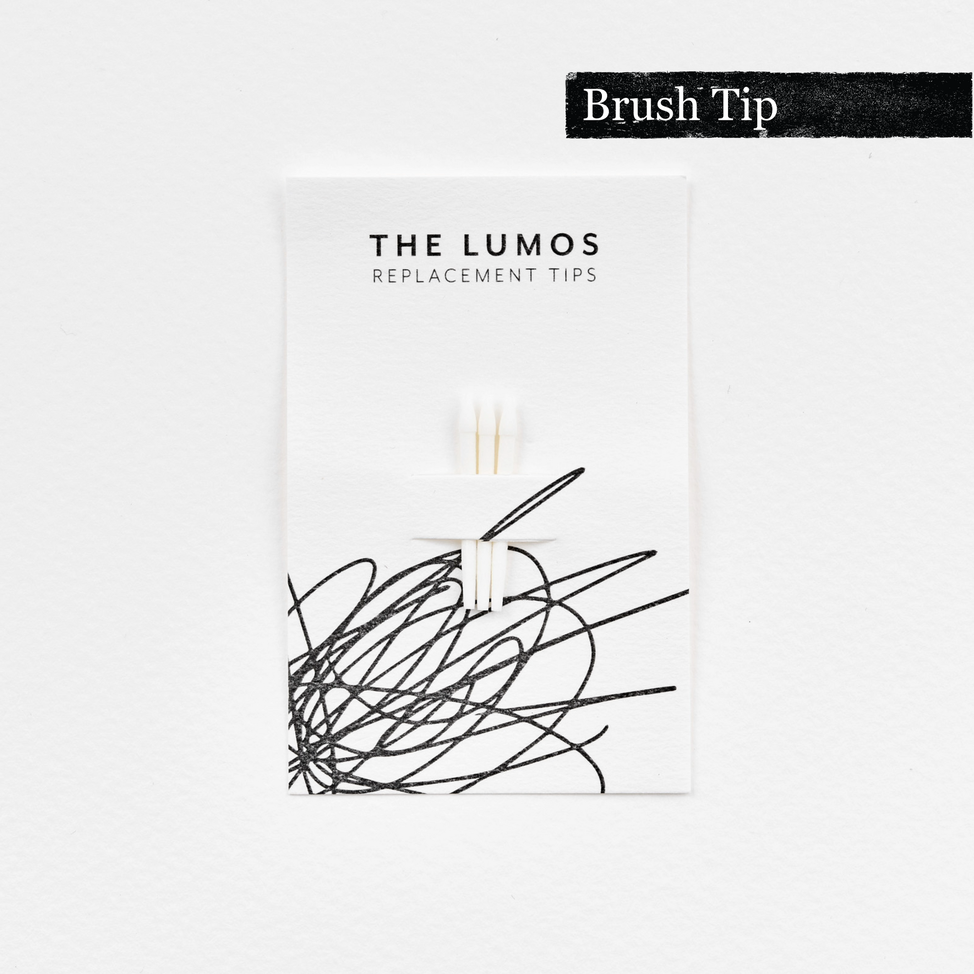 A pack of three Lumos replacement Brush tips attached to a white backing card. The card features &#39;THE LUMOS REPLACEMENT TIPS&#39; in uppercase black letters at the top, with an abstract black ink scribble design in the lower half. A black textured label in the upper right corner displays &#39;Brush Tip&#39; in white text. 