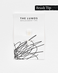 A pack of three Lumos replacement Brush tips attached to a white backing card. The card features 'THE LUMOS REPLACEMENT TIPS' in uppercase black letters at the top, with an abstract black ink scribble design in the lower half. A black textured label in the upper right corner displays 'Brush Tip' in white text. 