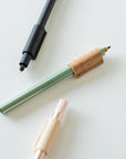 Handmade by Edward De Lacy, a pen grip and rollstop for the Lumos refillable pen – shown in black leather on the black Lumos, cork on the sage Lumos and natural leather on the rose gold Lumos