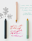 The Lumos Mini refillable pen (left to right) Black, Blush and Sage shown on samples of illustration and lettering creating using the interchangeable tips