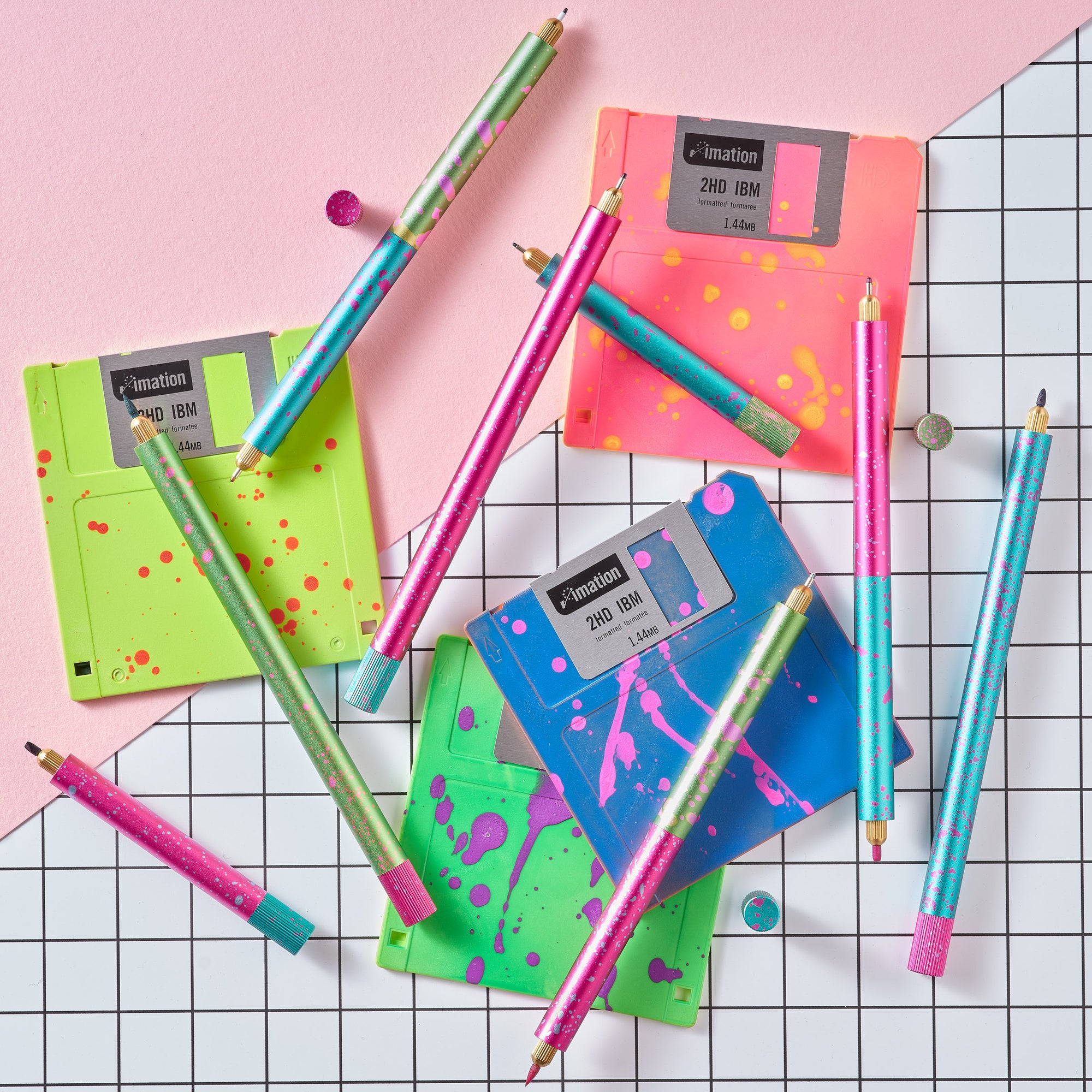 Flat lay of Lumos Splash pens in neon Appletini, Blue Raspberry, and Bubblegum colourways, styled with colourful floppy disks on a grid background.