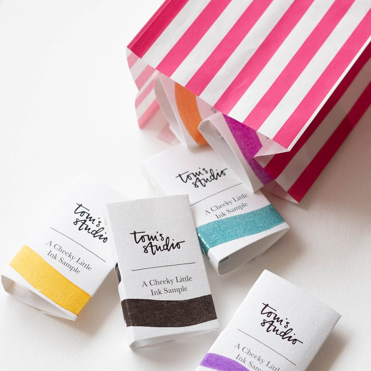 A selection of Tom's Studio Mini Fountain Pen Inks packaged in a candy-stripe paper bag