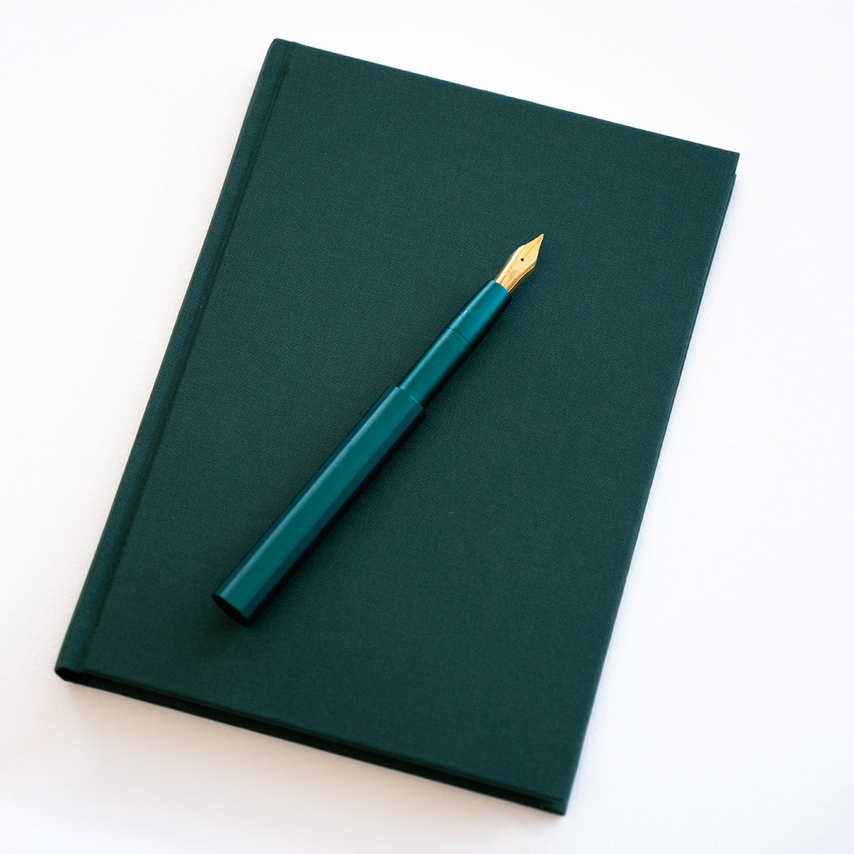 The Pocket Fountain Pen 2.0 in Ivy shown on a matching A5 Semikolon notebook in Forest