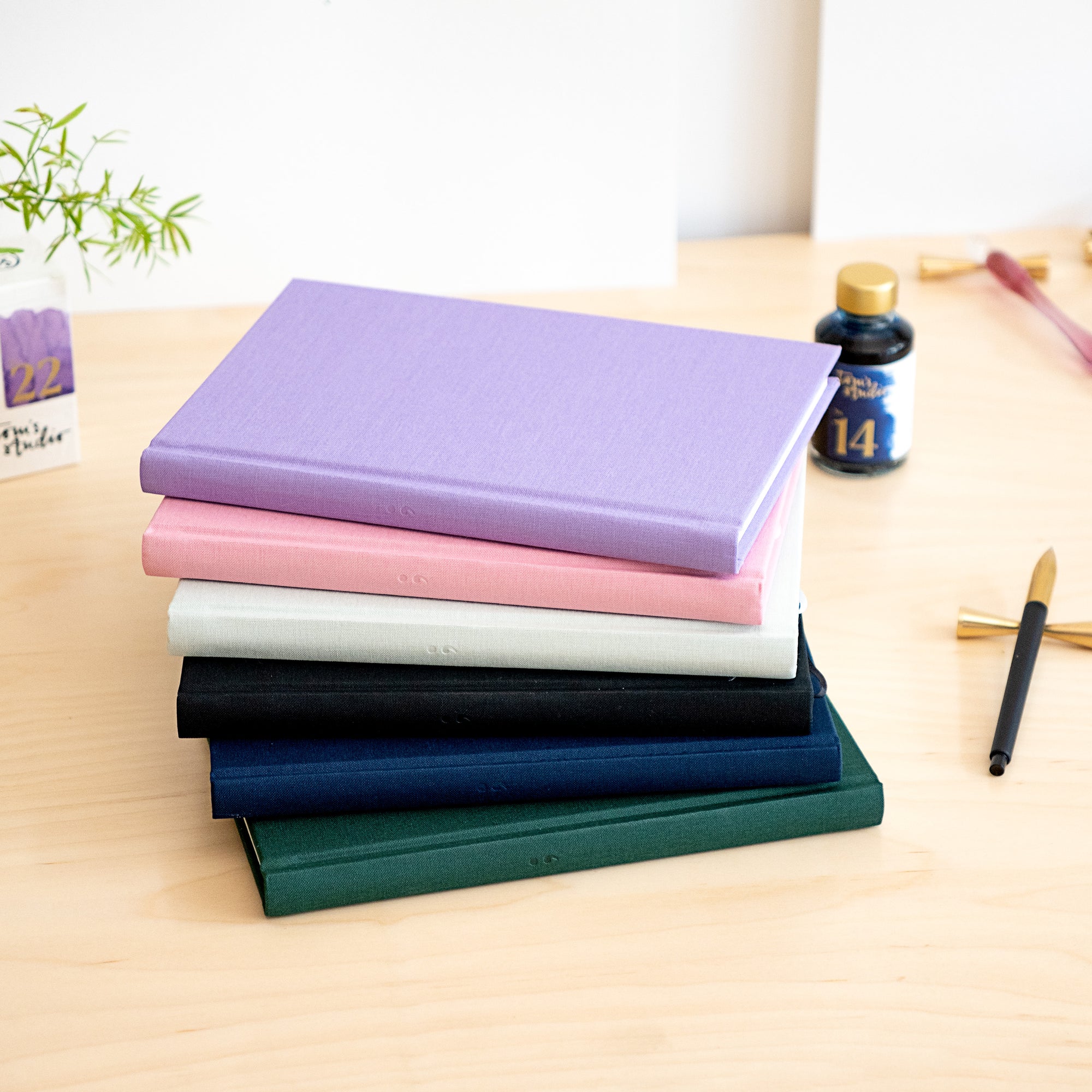 A stack of vibrant Semikolon A5 notebooks in various colours, with premium linen bound covers, displayed alongside drawing tools and ink.