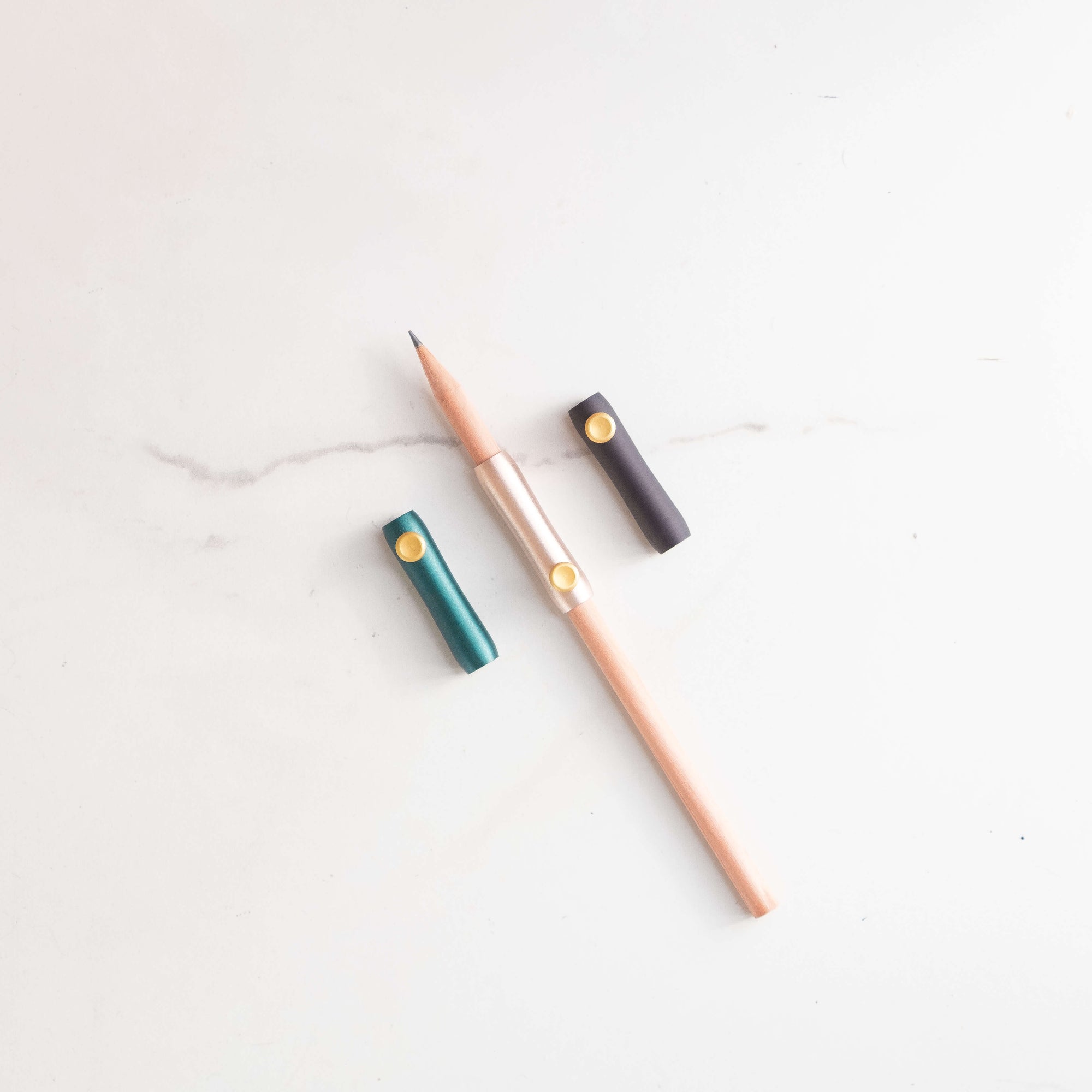 The Poise Pencil Grip Extender in (left to right) Ivy, Blush and Black. Shown on a standard pencil.