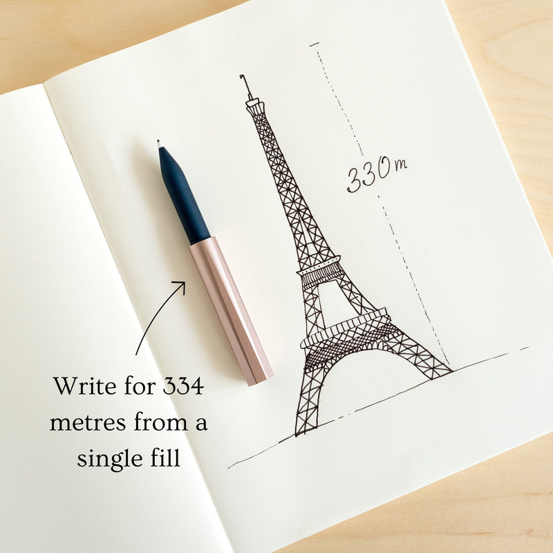 The Wren refillable everyday writing pen in Blush (lid) and Midnight (body) shown on an open notebook explaining that a single reservoir fill will write for 334 metres (the height of the Eiffel Tower)