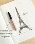 The Wren refillable everyday writing pen in Blush (lid) and Midnight (body) shown on an open notebook explaining that a single reservoir fill will write for 334 metres (the height of the Eiffel Tower)