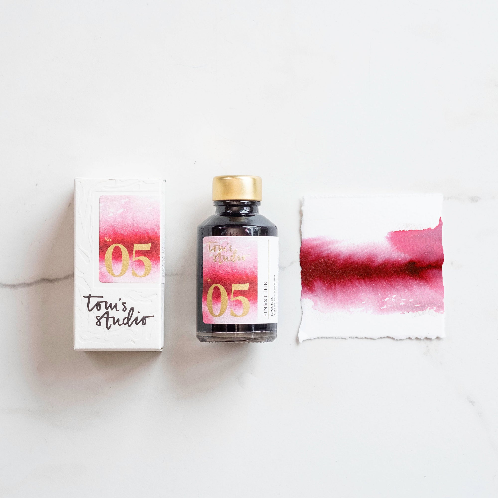 Tom's Studio Cassis Fountain Pen Ink with two pens with inky goodness on paper with an ink swatch demonstrating the colour
