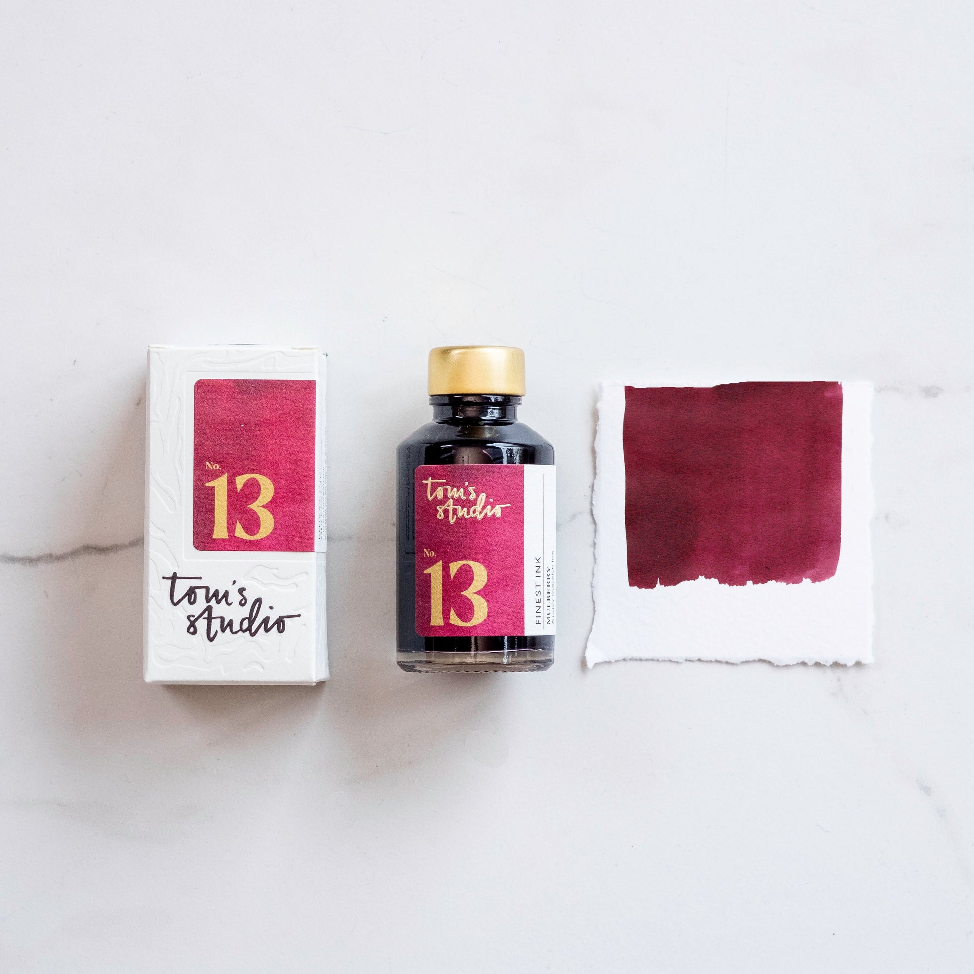 Tom's Studio Mulberry Fountain Pen Ink with two pens with inky goodness on paper with an ink swatch demonstrating the colour