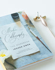 Modern Calligraphy - The Workbook by Imogen Owen book cover shown with the Carrot Calligraphy Pen and Butterfly Brass Pen Rest