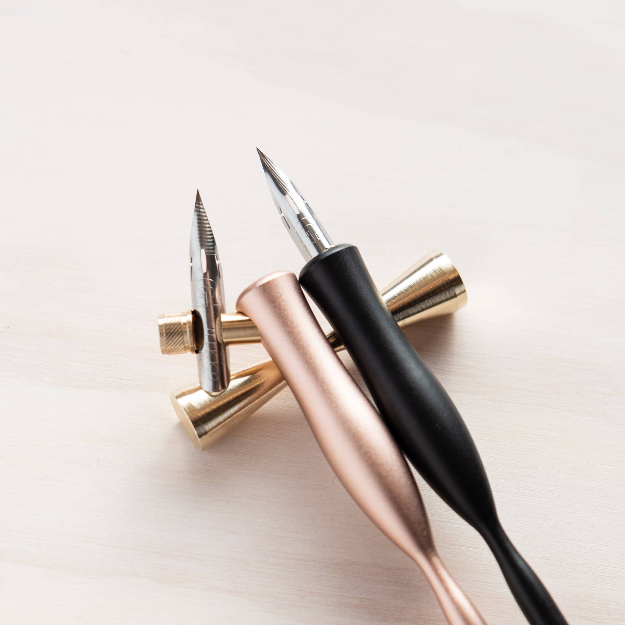 Butterfly brass pen rest with two calligraphy pens resting on it – one oblique, and one straight