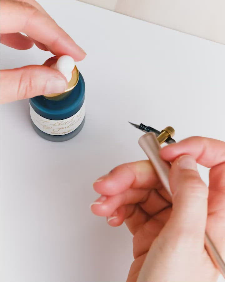 a calligraphy pen committing to paper in amethyst ink 