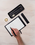 Writing in the black handmade leather journal with a fountain pen while a desk tray and pen rest store an oblique calligraphy pen