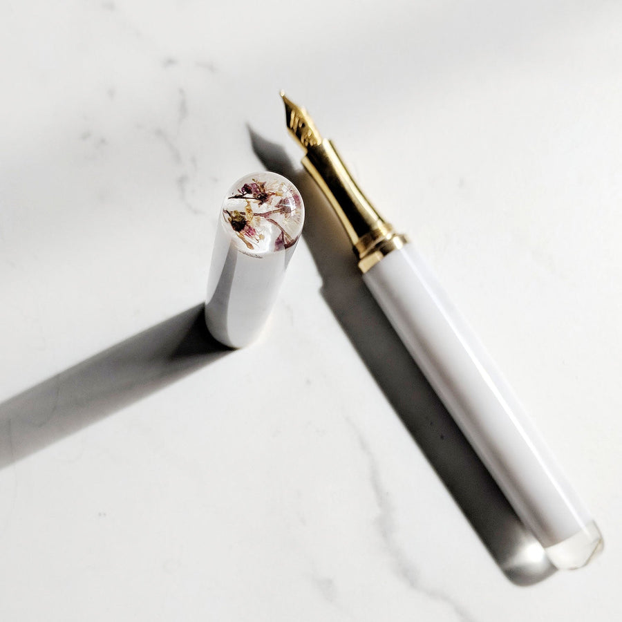 Encapsulated Flower Marble Studio fountain Pen on a white desk with dark shadows under the brass grip