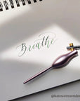 The Tom's studio flourish carrot calligraphy pen with oblique nib on a pad with breathe written on it