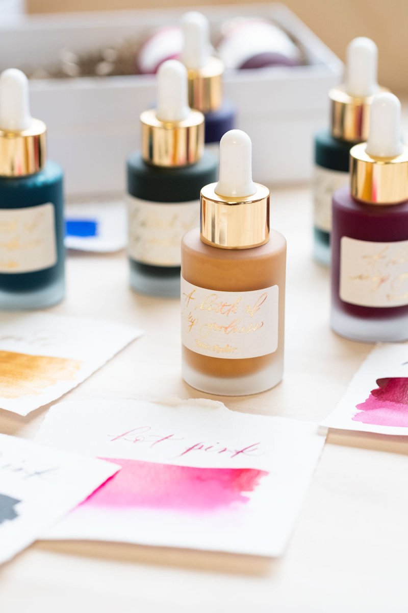 A selection of Tom&#39;s Studio Calligraphy inks on a desk with swatches showing their colours on the tabletop