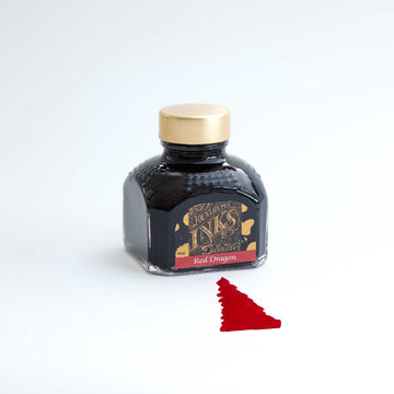 A bottle of red Dragon fountain pen ink on a white desk with some ink washed out to show the colour