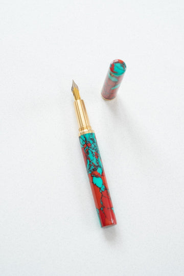 A red jasper Studio pen on a white desk with a flexible fountain pen nib