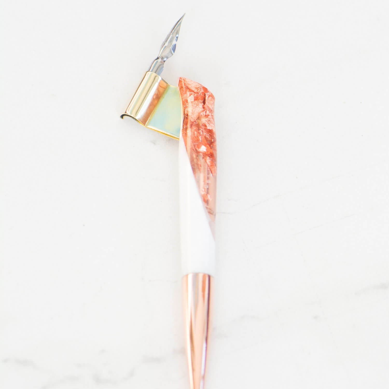 A close up of a rose gold and white oblique hand made calligraphy pen with a copper tail