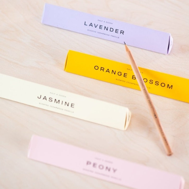 A scented pencil resting on the prism box packaging with the four different scents on display (top to bottom) Lavender, Orange Blossom, Jasmine and Peony