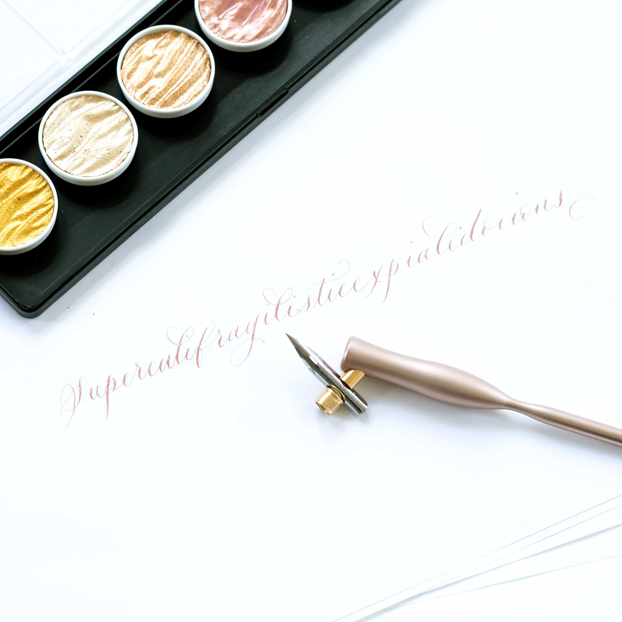 An oblique calligraphy pen in rose gold on paper with some modern calligraphy