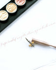 An oblique calligraphy pen in rose gold on paper with some modern calligraphy