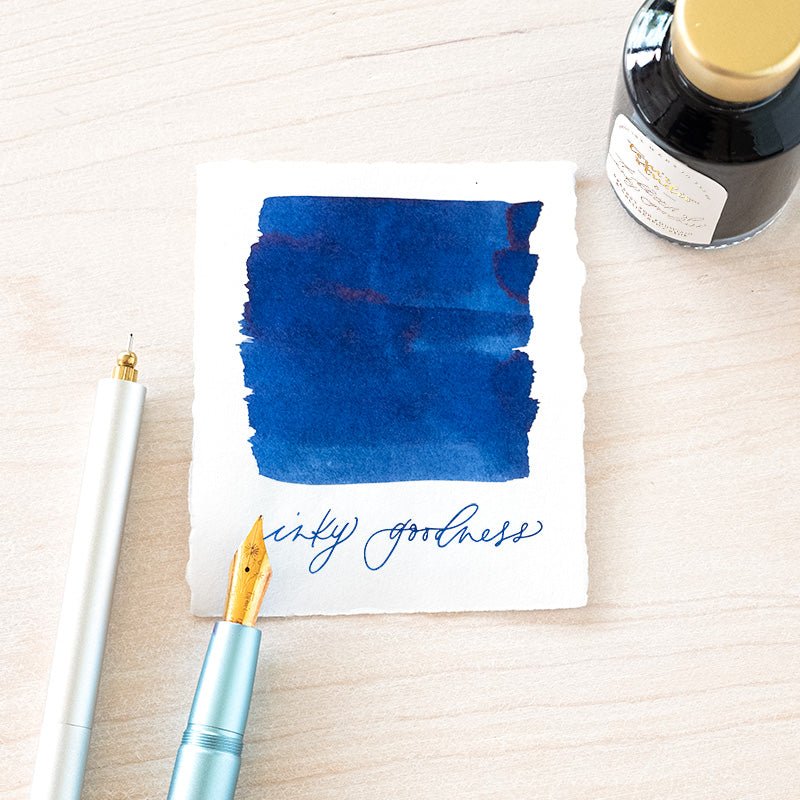 Tom's Studio Royal Blue Fountain Pen Ink with two pens with inky goodness on paper with an ink swatch demonstrating the colour